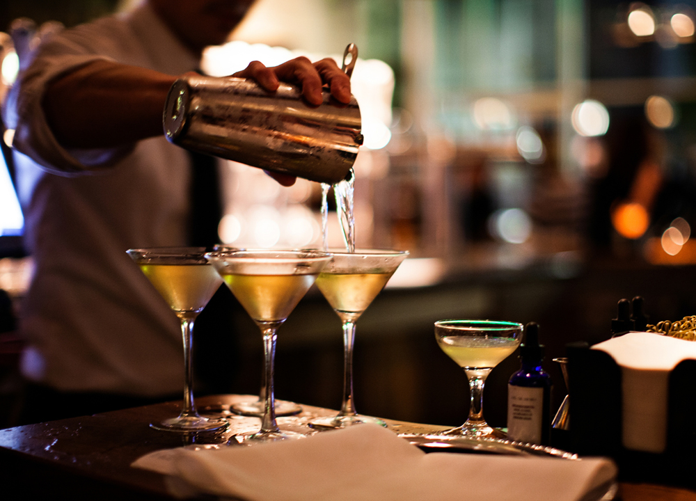 Bartender pouring drinks in martini glasses